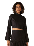 Paula Fashion House black linen mock-neck crop top with bell sleeves and button cuffs, paired with a ruffled skirt.