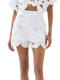 Paula Fashion House white high-waist shorts with floral cutwork and scalloped hem, worn by a model with a straw hat.